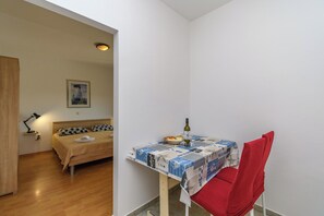 Ein Schlafzimmer mit einem Bett, einem Nachttisch mit Lampe, einem kleinen Tisch mit Flasche und Gläsern sowie einem roten Sessel.