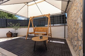 A patio with a swing, a round table with two bottles, a potted plant, and a stone wall. - House Mirakul Near Krka With Private Pool (Skradin)