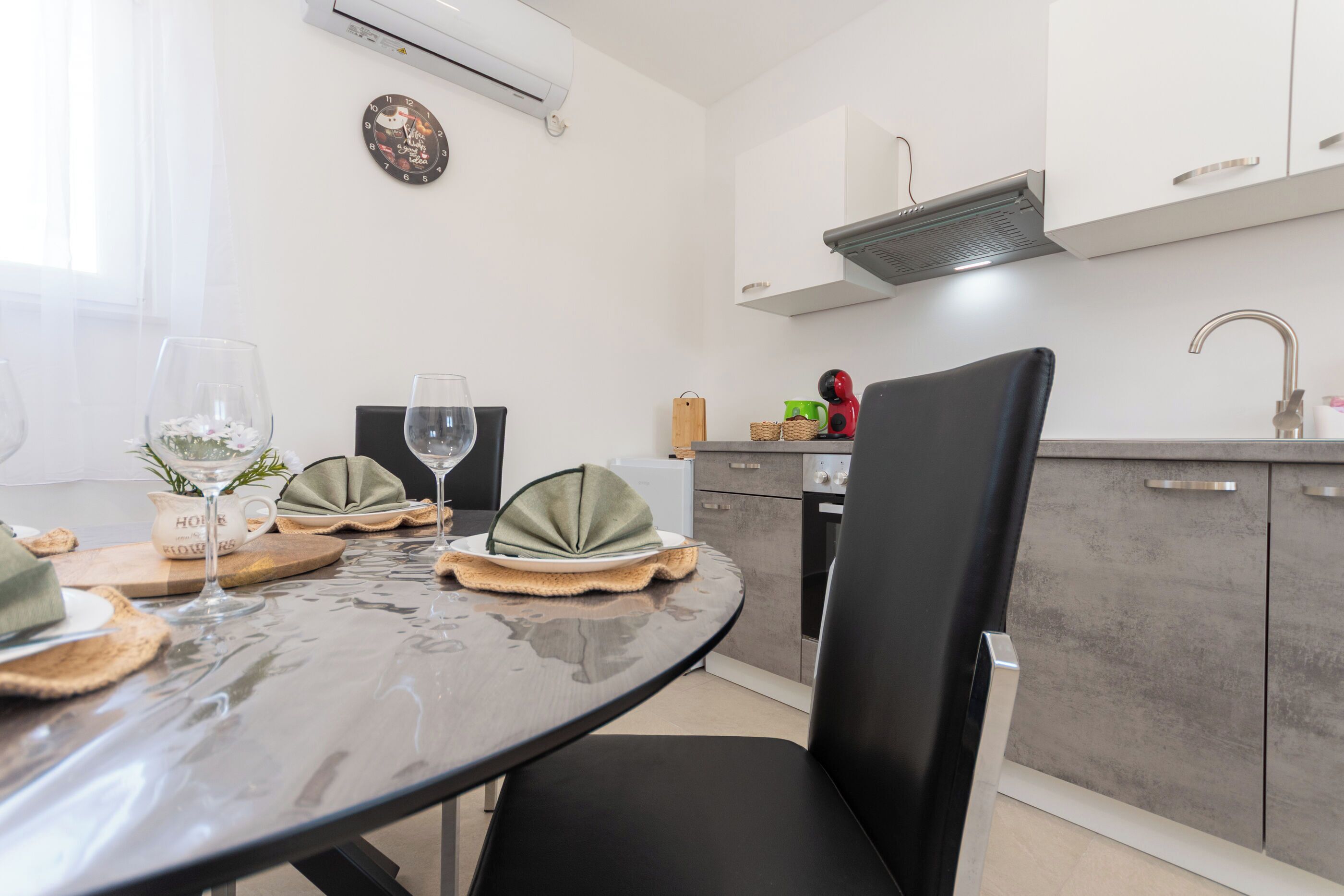 A modern kitchen with a dining area, featuring a round table, chairs, and a clock on the wall.