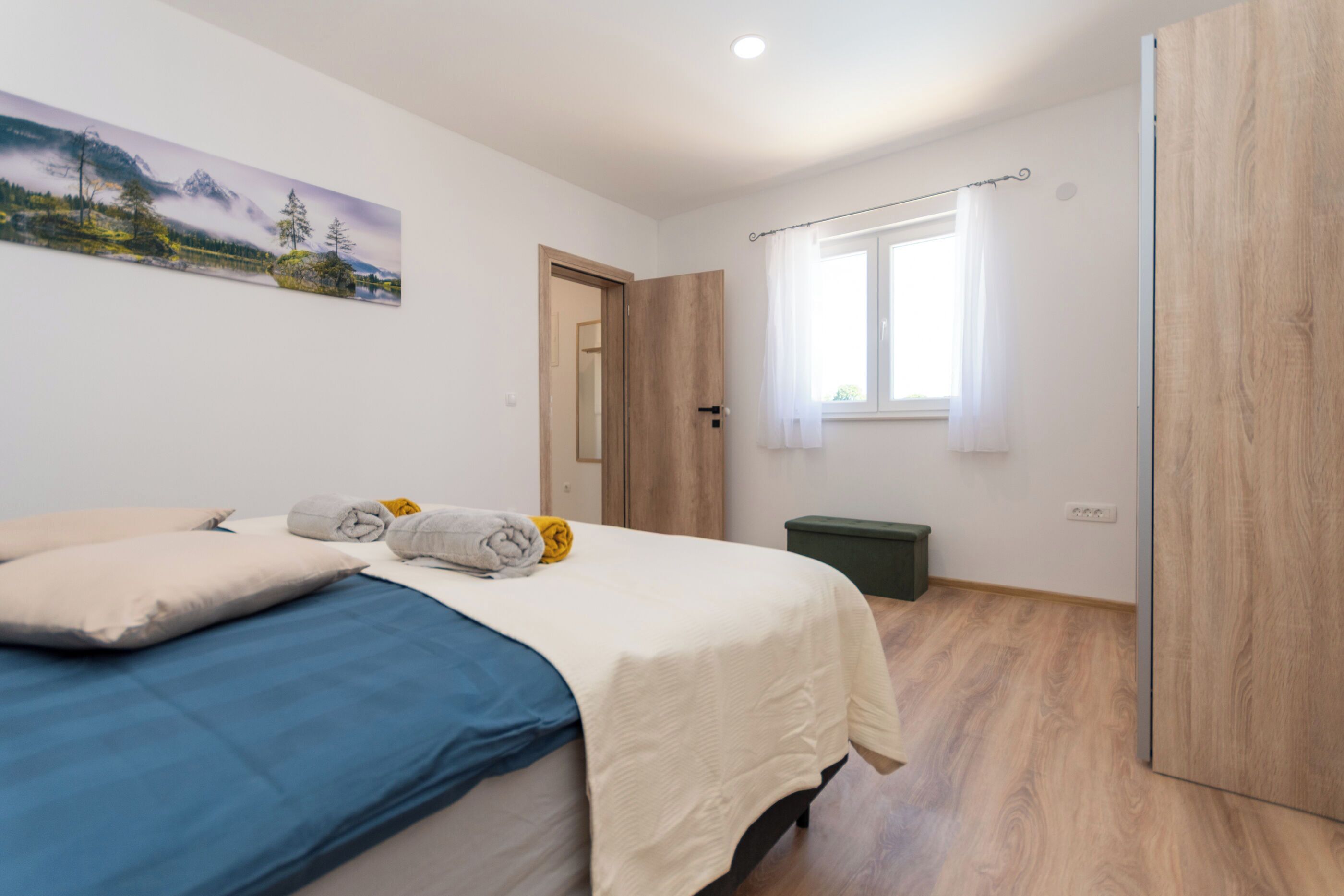 A bedroom with a bed, a window, a door, and a painting on the wall.