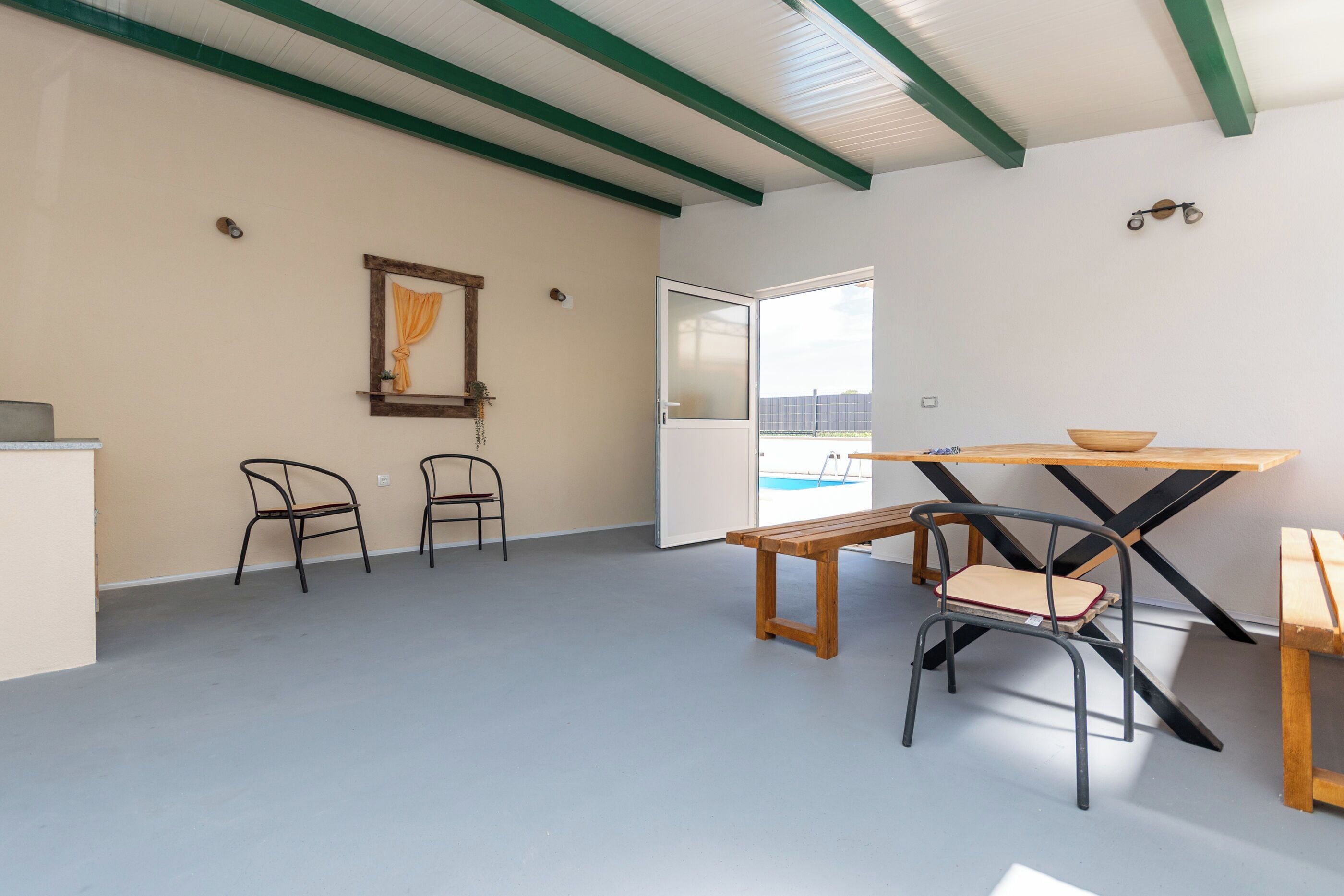 A room with a wooden table, two chairs, a bench, and a door leading outside.