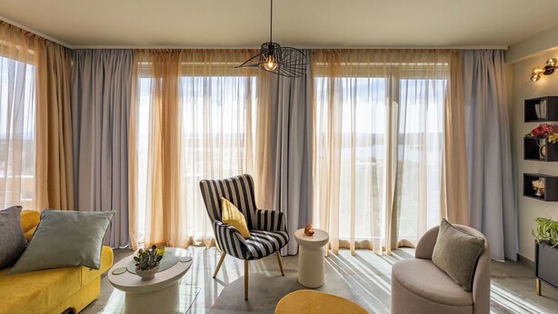 A modern living room with a striped armchair, a round side table, a sofa, and a large window with sheer curtains. - Apartments Menigo Manzoni (Punat)
