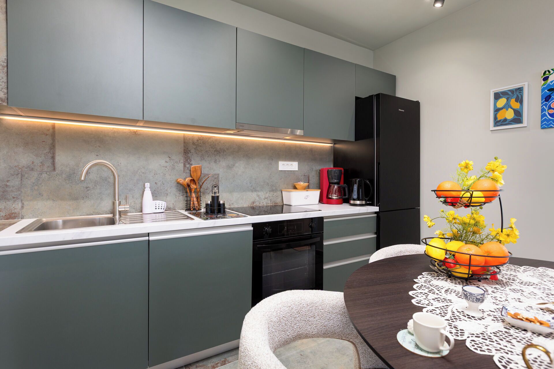 A modern kitchen with grey cabinets, a stainless steel sink, a coffee maker, and a fruit bowl on the counter.