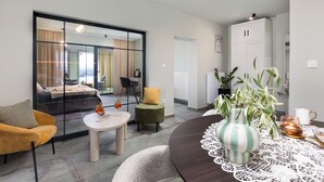 A modern living room with a sofa, a round table, and a dining table with a lace tablecloth. - Apartments Menigo Manzoni (Punat)