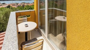 A balcony with a table and chairs, a sliding glass door, and a view of a coastal town. - Apartments Menigo Manzoni (Punat)