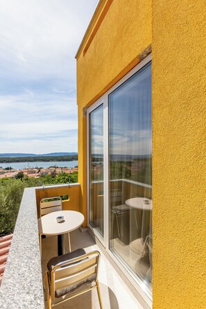 Ein Balkon mit Tisch und Stühlen, eine Schiebetür und Blick auf eine Küstenstadt.