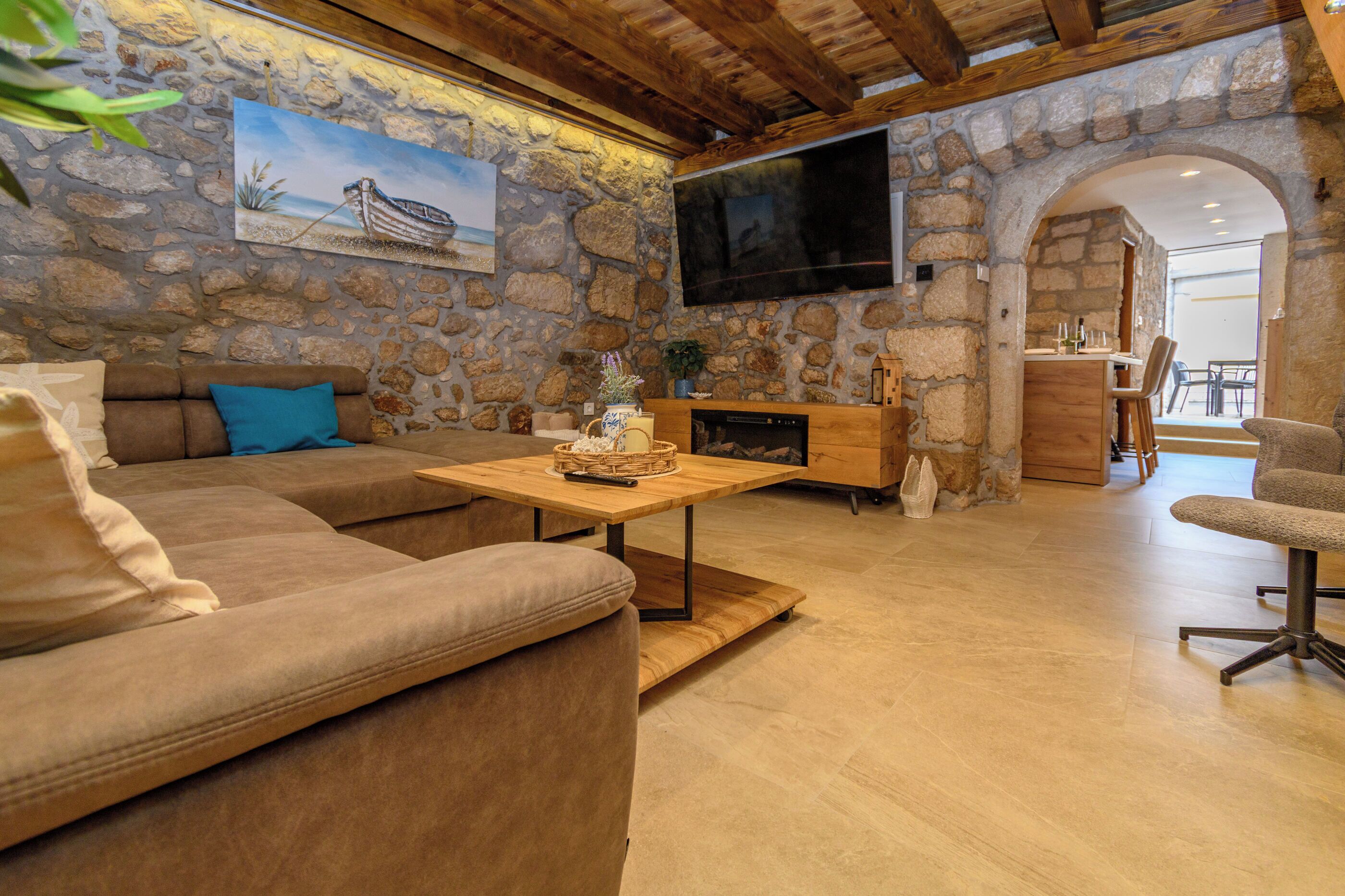 Un salón con paredes de piedra, un sofá, una mesa de centro, televisor, chimenea y un arco que conduce a un comedor.