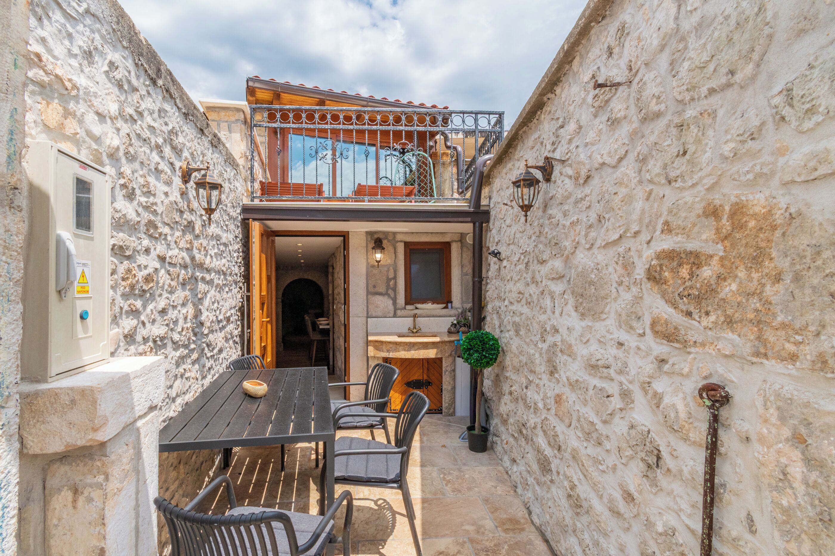 A stone-walled building with a balcony, a dining area with chairs and a table, and a small kitchen area.
