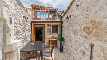 A stone-walled building with a balcony, a dining area with chairs and a table, and a small kitchen area.