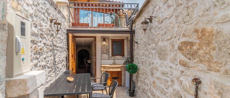 A stone-walled building with a balcony, a dining area with chairs and a table, and a small kitchen area.