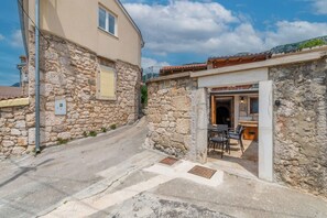 A narrow street with a stone building, a small outdoor seating area with chairs and a table, and a clear sky. - House Villa Lara (Vinodol)