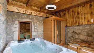 A wooden interior with a stone wall, a wooden cabinet, and a hot tub.