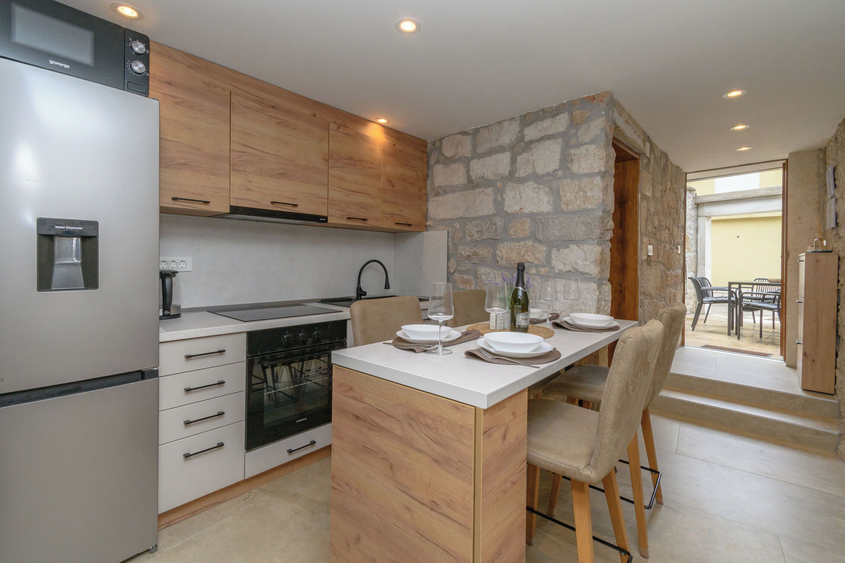 A modern kitchen with wooden cabinets, a built-in oven, and a dining area with a stone accent wall.