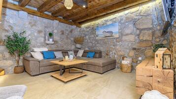 A stone-walled room with a wooden ceiling, a sofa, a coffee table, and a cabinet with a small house model.