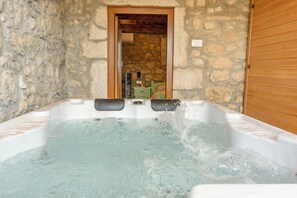 Une pièce aux murs de pierre, avec une porte en bois, une baignoire remplie de mousse et une petite table de chevet.