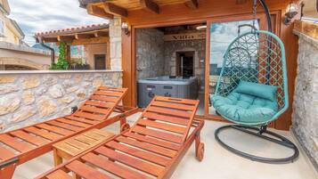 A wooden deck with lounge chairs and a hanging chair, a stone wall, and a sign that reads 'Villa.'