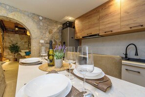 Un coin repas agrémenté d’un mur en pierre, de meubles en bois et d’une table dressée pour deux personnes, avec assiettes, verres et couverts.
