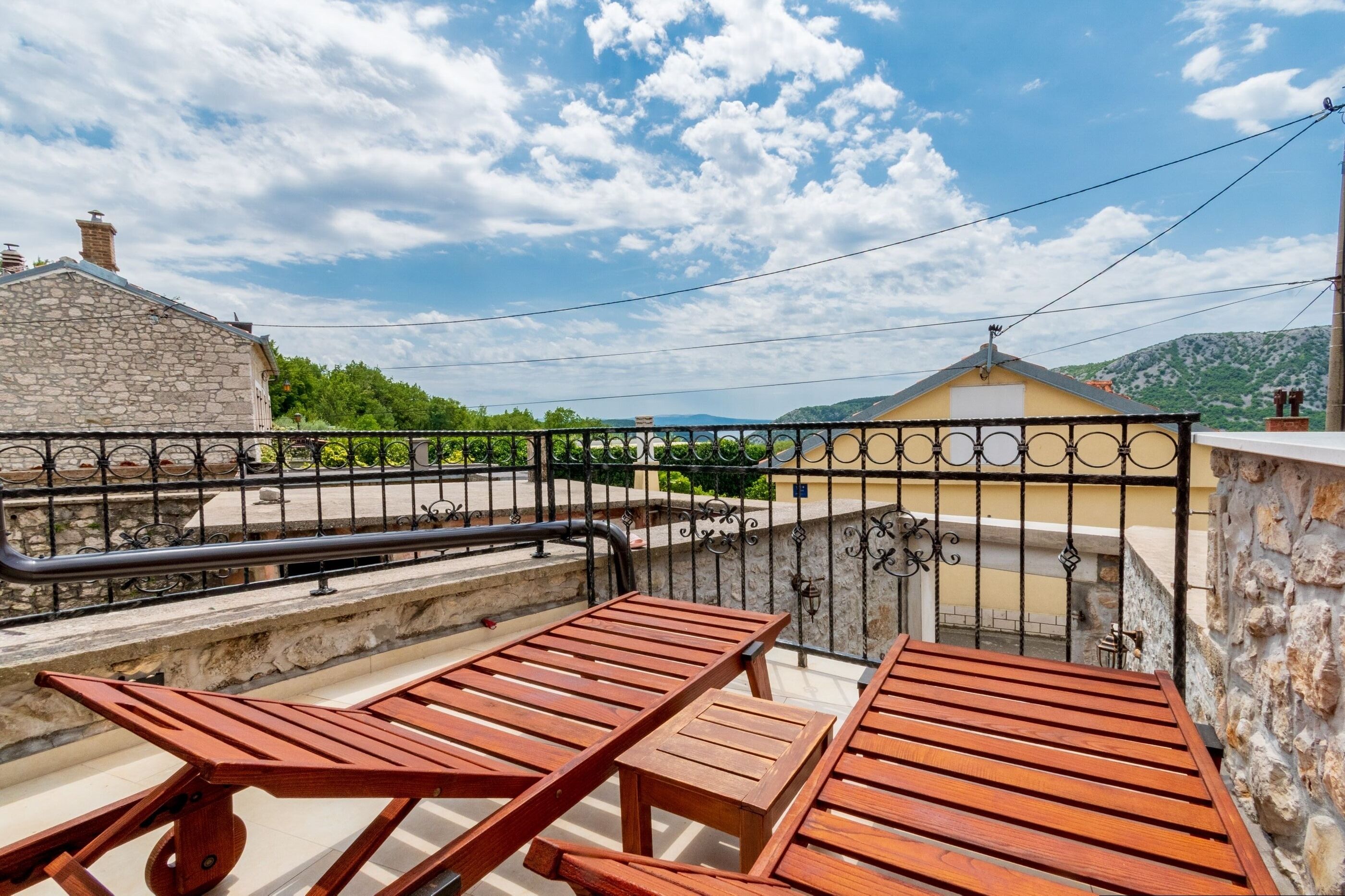 Un balcon doté de meubles en bois, d’un mur en pierre et offrant une vue sur une montagne.