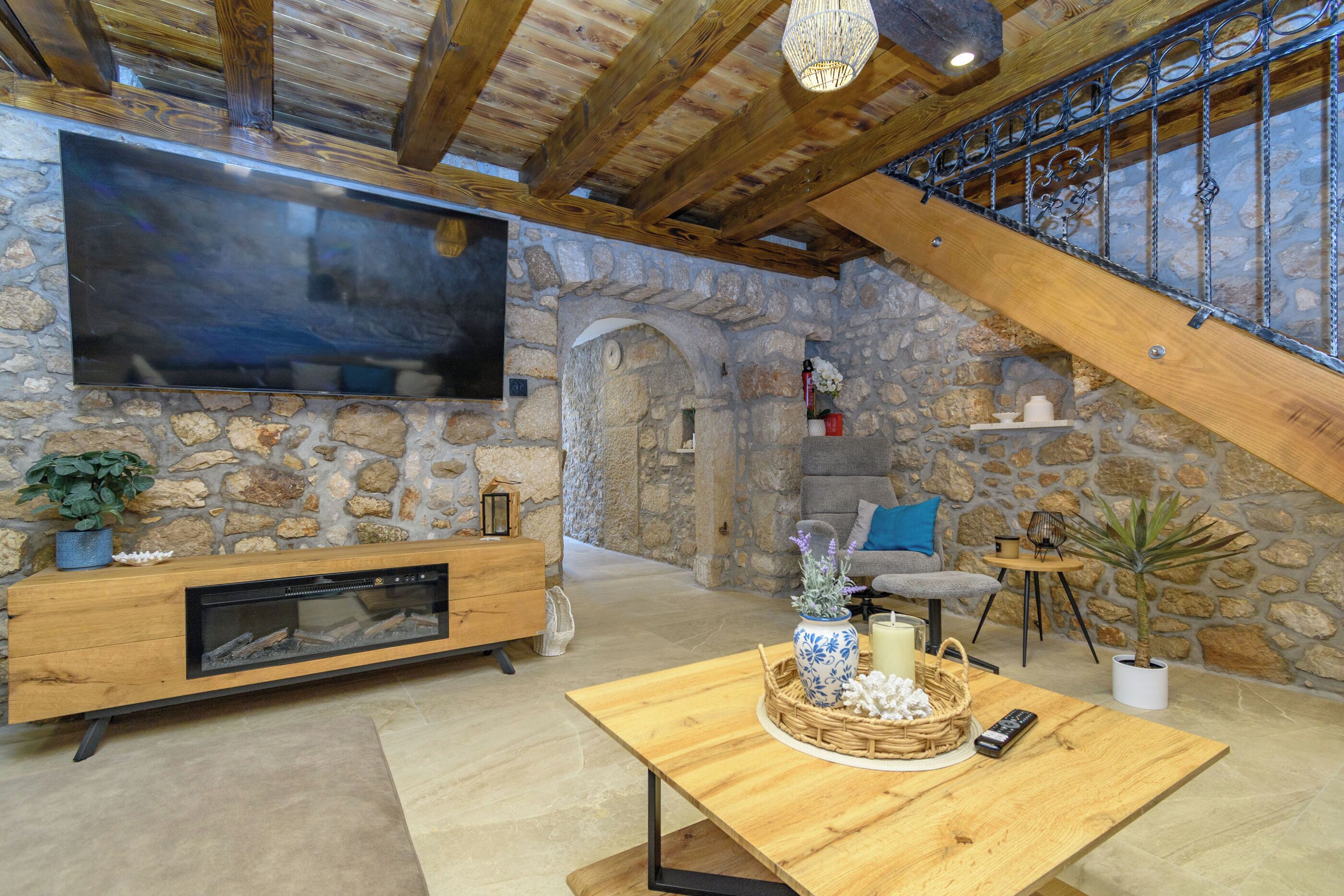 A spacious living area with a stone wall, wooden furniture, a fireplace, and a large flat-screen TV.