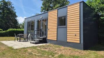 Un bâtiment moderne de plain-pied, avec une façade combinant verre et bois, un patio doté de sièges extérieurs et un ciel dégagé.