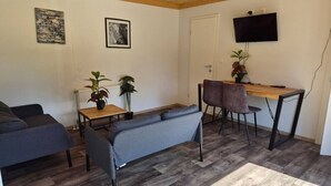 A living room with a sofa, a table, and a TV mounted on the wall. - Cube chalet voor 4 personen | De Otterberg (Wijster)