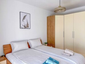 A double bed with white bedding, a wooden headboard, a bedside table, a hanging light fixture, a wardrobe, and a framed picture on the wall. - Apartment Mediterranean (Opatija)