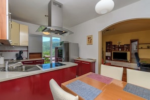 Eine moderne Küche mit einer zentralen Kochinsel, ein Essbereich mit Tisch und Stühlen sowie ein Blick ins Freie.