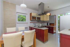 Une cuisine moderne dotée d’un îlot central, de meubles de rangement intégrés et d’une fenêtre donnant sur un espace verdoyant.