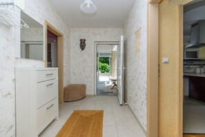 A narrow hallway with a white cabinet, a brown ottoman, and a door leading to a kitchen area. - Apartment Mediterranean (Opatija)