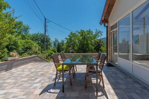 An outdoor patio with a glass table and wicker chairs, surrounded by a stone-tiled floor and lush greenery. - Apartment Mediterranean (Opatija)