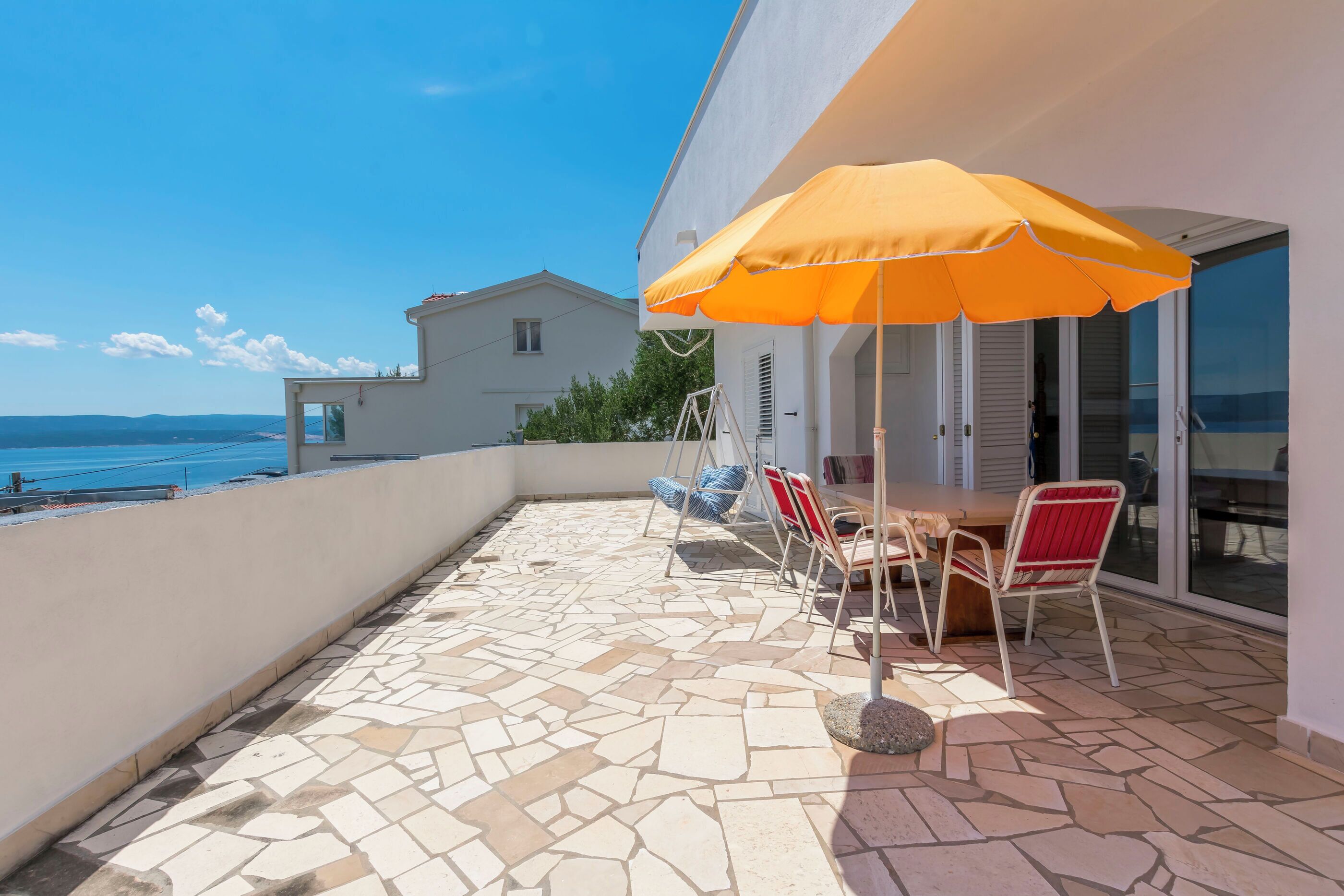 A patio with a table and chairs, a swing chair, and a view of the sea.