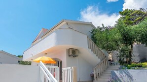 A white building with a curved facade, a staircase, and a yellow umbrella. - Apartment Sunny (Omis)