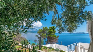 A coastal view with a staircase leading to a building, a garden with plants, and a clear blue sea. - Apartment Sunny (Omis)