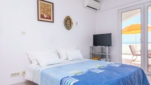A bedroom with a bed, a television on a stand, a painting, and a view of the sea through a glass door. - Apartment Sunny (Omis)