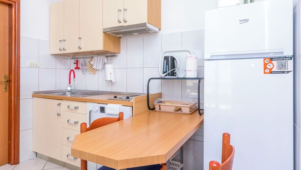 A kitchen with a wooden table, beige cabinets, a white refrigerator, and a toaster. - Apartment Sunny (Omis)