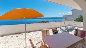 A patio with a table, chairs, an orange umbrella, and a swing chair overlooking a sea view. - Apartment Sunny (Omis)
