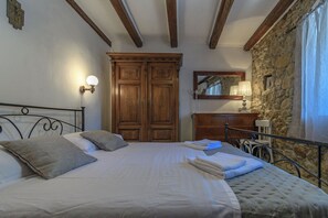 A bedroom with a bed, wooden wardrobe, a mirror, and a stone wall. - House Vila Ana (Lopar)