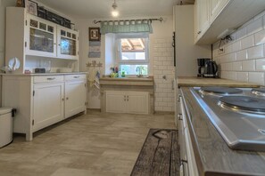 A kitchen with white cabinets, a wooden bench, a stove, and a window with a view. - House Vila Ana (Lopar)