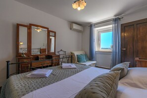A bedroom with a bed, a dresser, a mirror, a window with curtains, and an air conditioning unit. - House Vila Ana (Lopar)