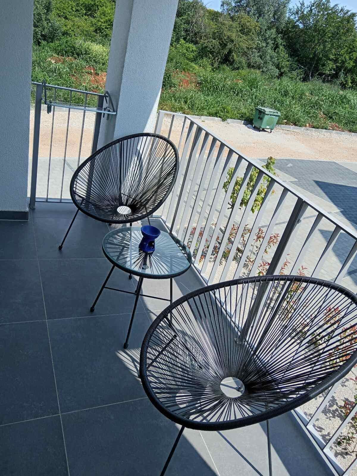 Ein Balkon mit zwei schwarzen Stuhlgestellen aus Drahtgitter, einem kleinen runden Tisch und einer blauen Schüssel.