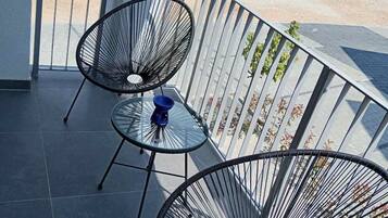 Ein Balkon mit zwei schwarzen Stuhlgestellen aus Drahtgitter, einem kleinen runden Tisch und einer blauen Schüssel.