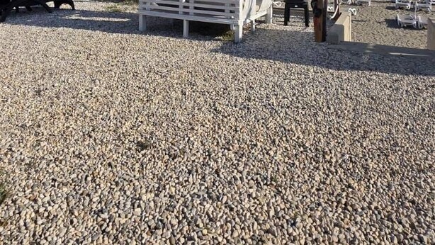 Ein Strand mit einer weißen Struktur, möglicherweise ein Kiosk, und einem Surfbrett, das dagegen lehnt.