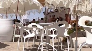 Sitzgelegenheiten im Freien mit weißen Stühlen und Spitzenschirmen, ein Gebäude im Hintergrund und ein klarer Himmel.