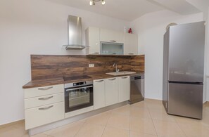 A modern kitchen with a stainless steel refrigerator, built-in oven, and white cabinetry. - Apartment Villa Dijana (Vodice)