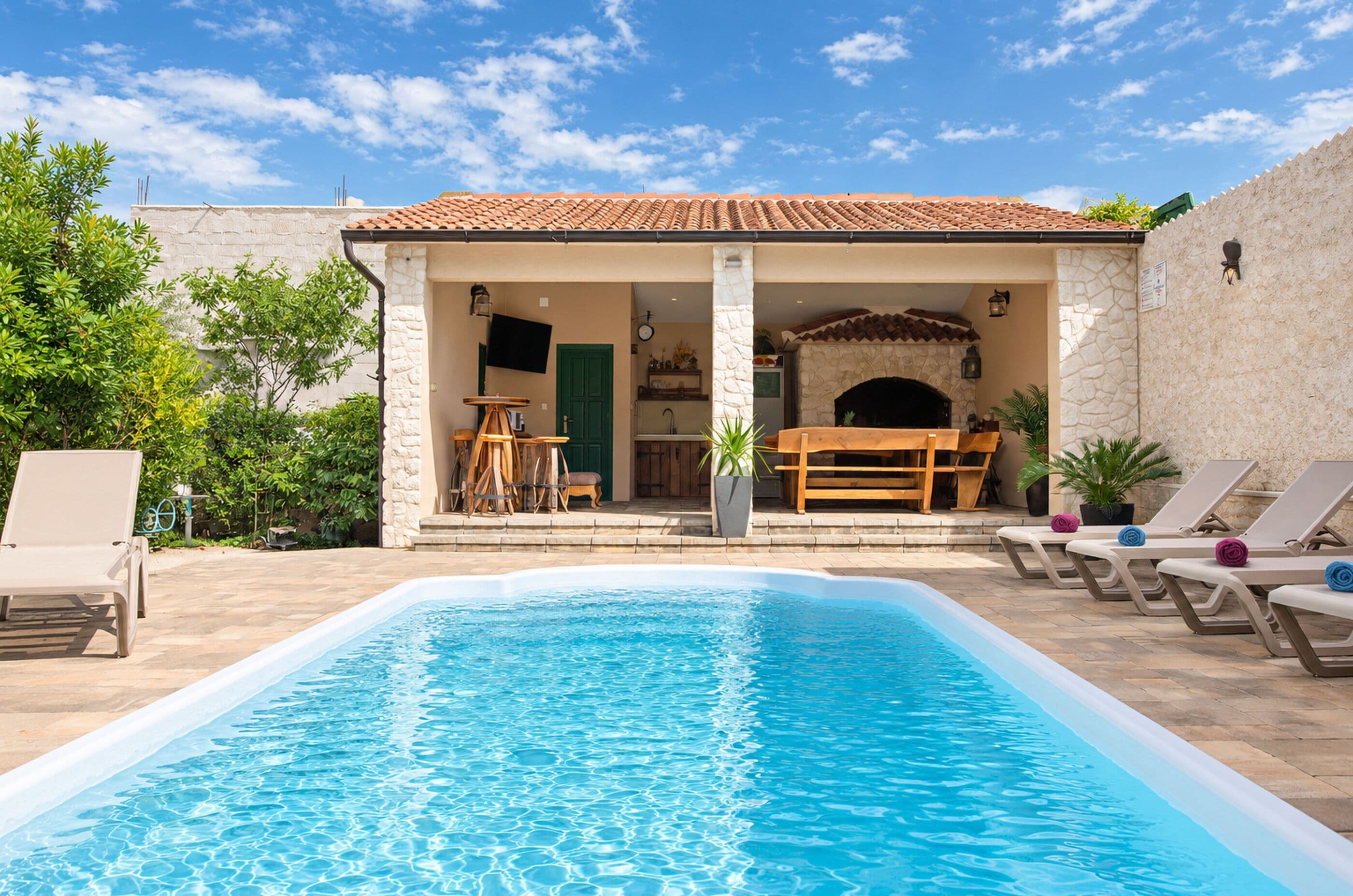 Ein Swimmingpool mit Liegestühlen und einer überdachten Terrasse mit Kamin.