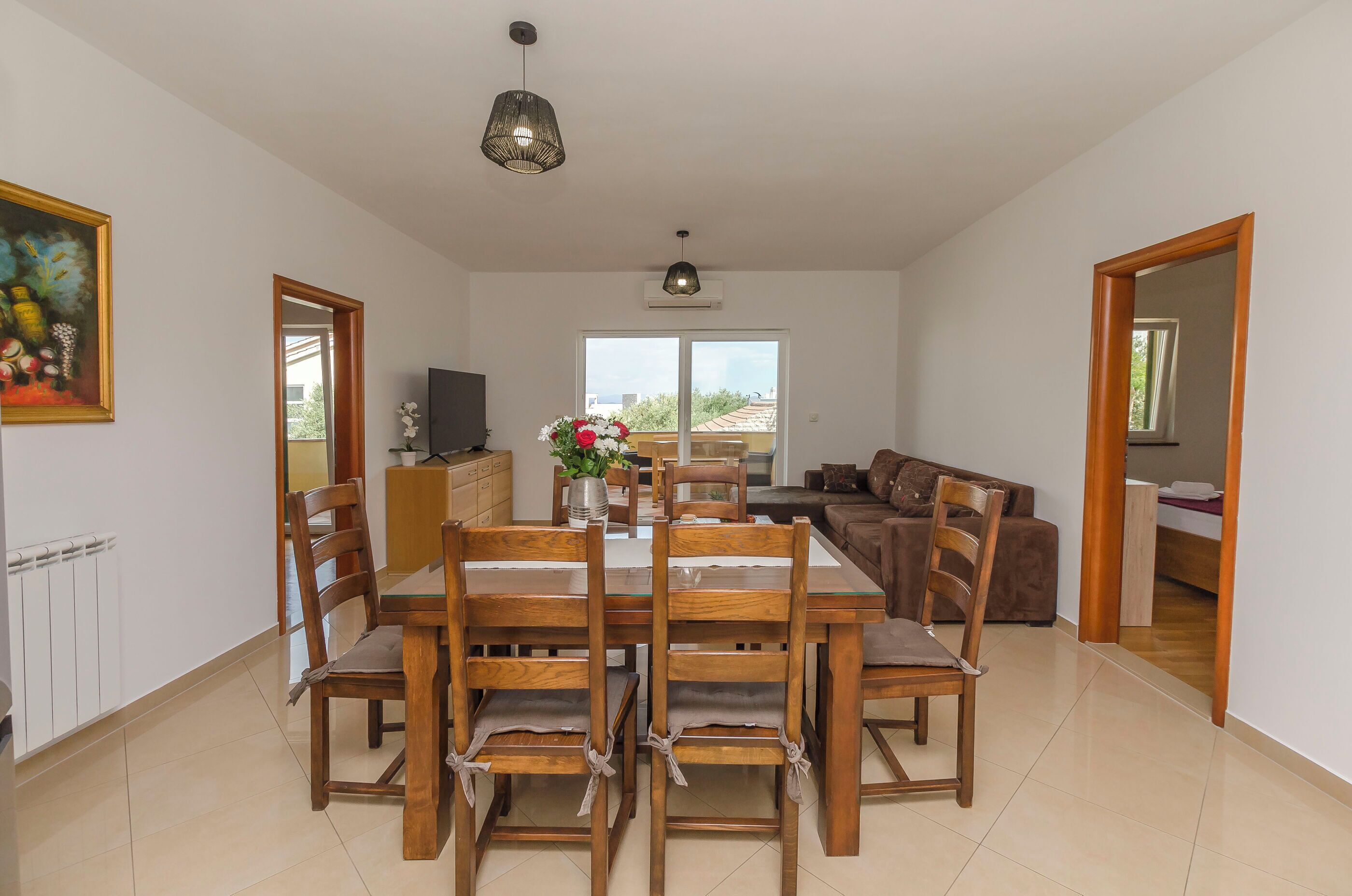 A dining area with a wooden table and chairs, a TV, and a flower vase.