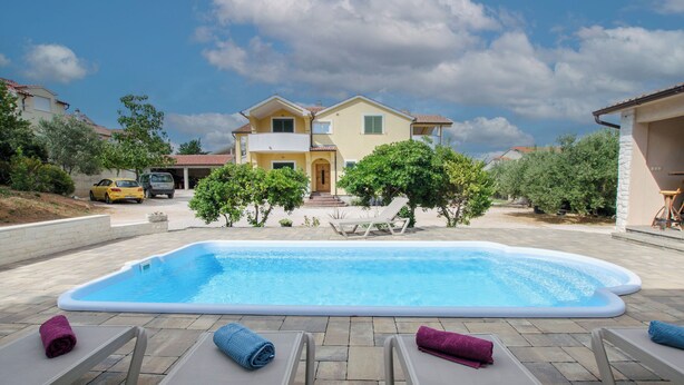 Ein Swimmingpool mit Liegestühlen und Handtüchern, umgeben von einem Haus und Grünflächen.