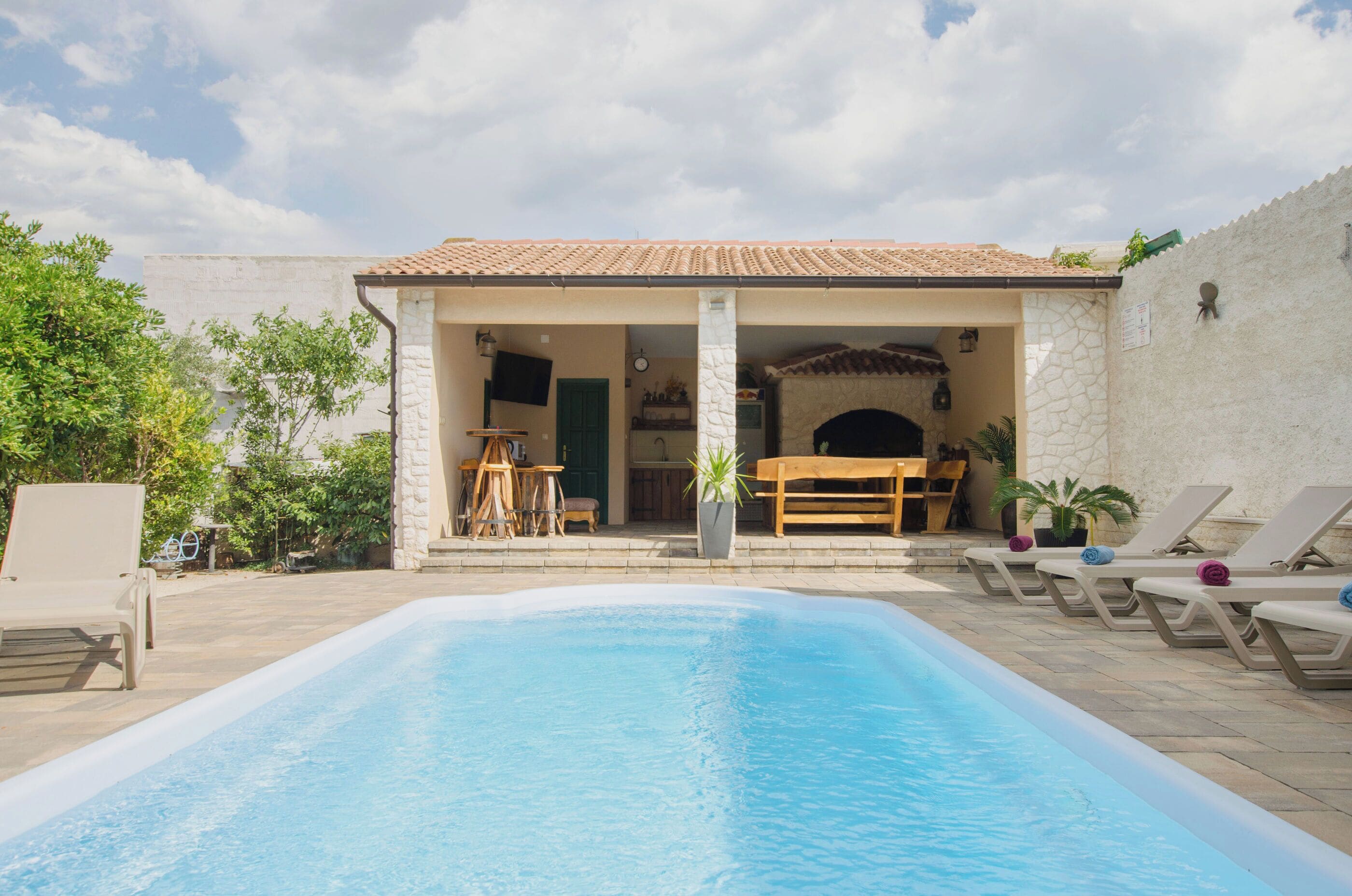 A swimming pool with lounge chairs, a covered seating area, and a stone wall.