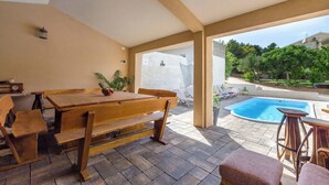 Ein Holztisch und Bänke in einem überdachten Außenbereich, im Hintergrund ein Pool.