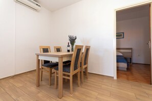 Ein Zimmer mit einem Holztisch, Stühlen, einer kleinen Vase mit Blumen und einem Stockbett im Hintergrund.